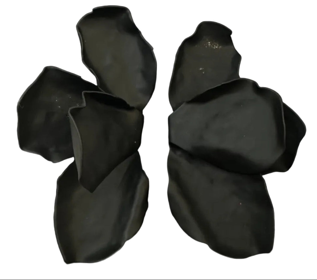 A black, abstract flower-shaped sculpture resembling Kybalion Jewellery’s Bougainvillea Earrings in various colours is displayed on a square base atop a light surface.