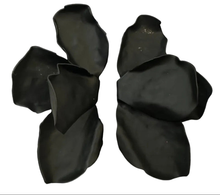 A black, abstract flower-shaped sculpture resembling Kybalion Jewellery’s Bougainvillea Earrings in various colours is displayed on a square base atop a light surface.