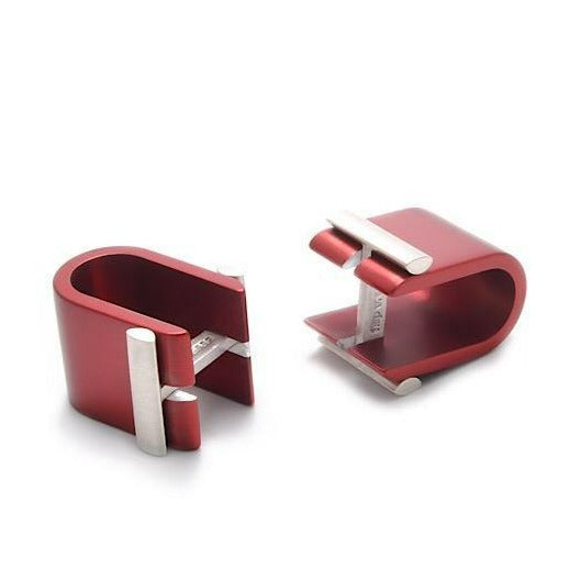 Two red rectangular Affinor Wrap Around Cufflinks by Filip Vanas made of anodized aluminum with smooth, polished surfaces. Each cufflink has a sterling silver accent bar running across the top, forming a modern and sleek design reminiscent of innovative napkin holders. The cufflinks are placed side by side, one standing upright and the other lying down.