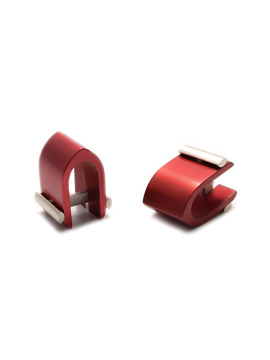 A pair of Ogive Wrap Around Cufflinks by Filip Vanas with a sleek, curved design. Each features a polished sterling silver bar running through the middle, providing a striking contrast with the vibrant red. The design is contemporary, minimalistic, and elegant—an innovative concept in accessory fashion.