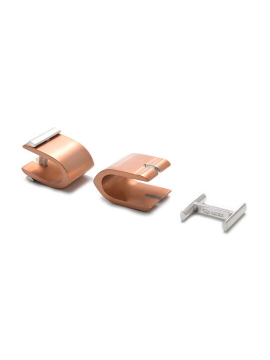 A pair of copper-colored Ogive Wrap Around Cufflinks by Filip Vanas featuring a sleek, modern design. One cufflink is positioned right-side up, showcasing its curved 'S' shape, while the other is disassembled to reveal the sterling silver locking mechanism. This innovative concept perfectly blends style with functionality.