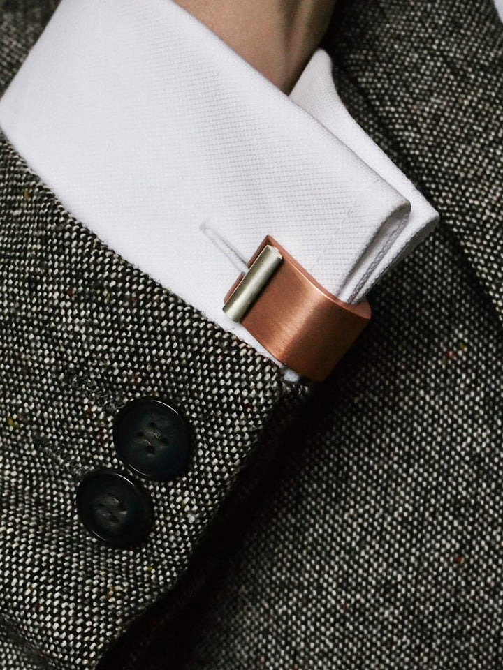 Close-up of a person wearing a gray tweed jacket with black buttons, a white dress shirt, and sterling silver cuff links. The Ogive Wrap Around Cufflinks by Filip Vanas have a modern, minimalist design and secure the neatly folded shirt cuff.