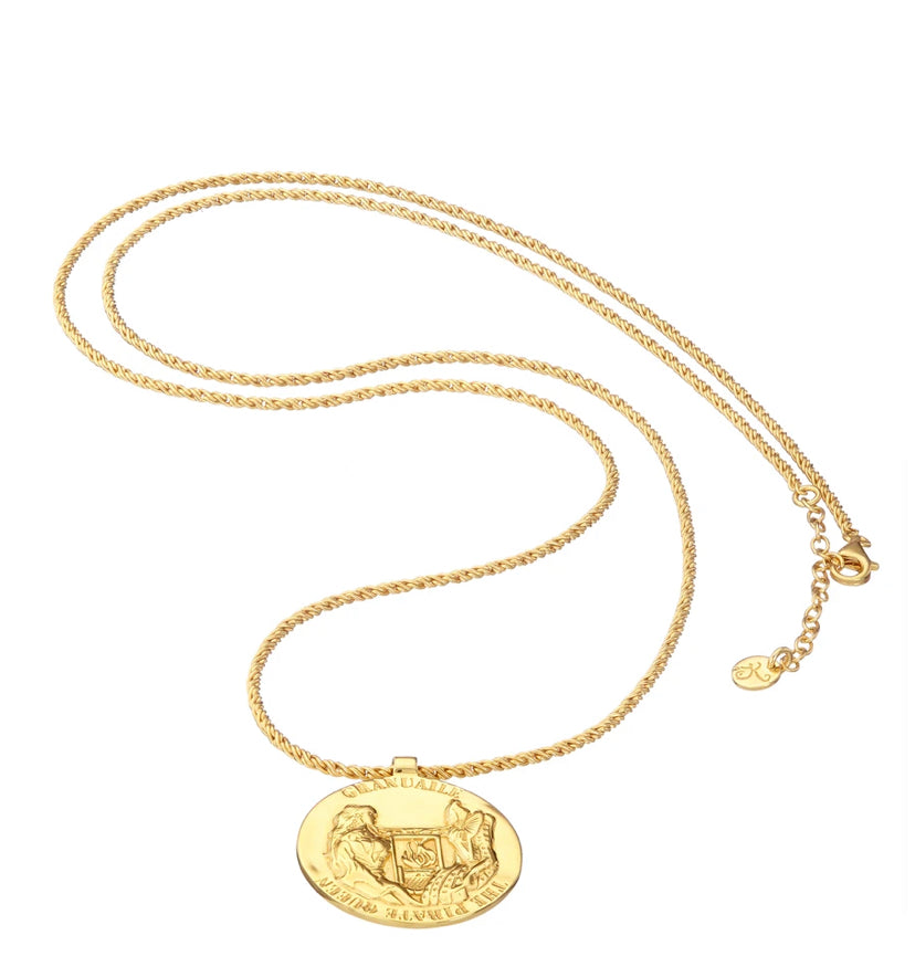 The Grace O'Malley Medallion Small by Jennifer Kinnear is a gold-plated silver necklace featuring a round pendant with an intricate design. The pendant showcases embossed historical imagery, including eagles and lions in shield emblems, along with the text "Dominus Illuminatio Mea." The chain is equipped with a lobster clasp and includes a circular tag.