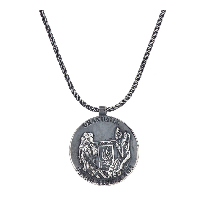 The Grace O'Malley Medallion Small by Jennifer Kinnear features a round pendant with intricate engraving of two figures: a seated person and a standing winged figure, accompanied by a harp and other detailed elements reminiscent of the Granuaile medallion. The word "OMNIA" is inscribed at the top of the gold-plated silver necklace.