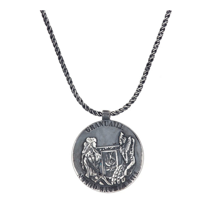 The Grace O'Malley Medallion Small by Jennifer Kinnear features a round pendant with intricate engraving of two figures: a seated person and a standing winged figure, accompanied by a harp and other detailed elements reminiscent of the Granuaile medallion. The word "OMNIA" is inscribed at the top of the gold-plated silver necklace.