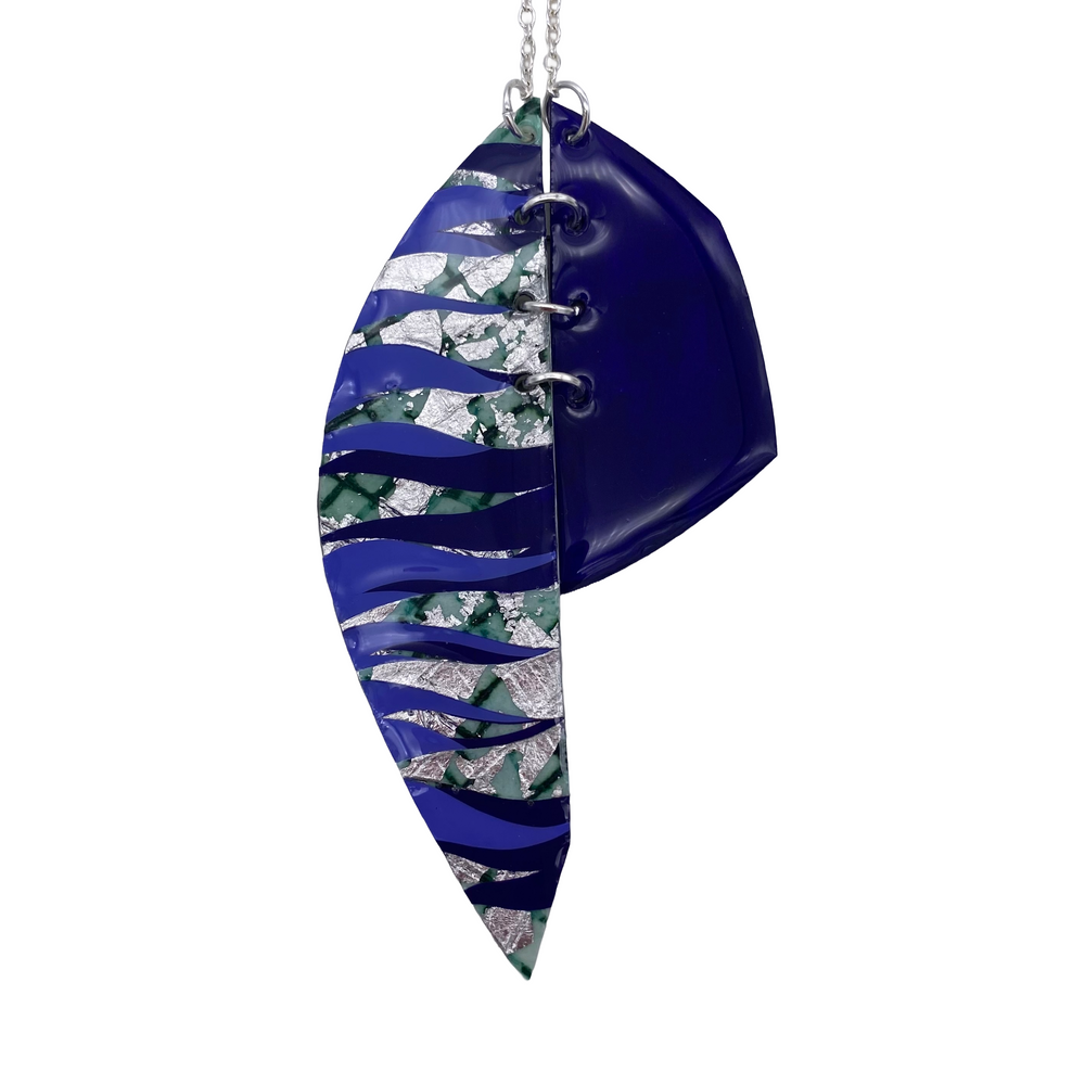 The Rothlú Easca Sgraffito Necklace features two overlapping, eco resin leaf-shaped pendants in celadon, silver, cornflower, and midnight blue, suspended from a silver chain.