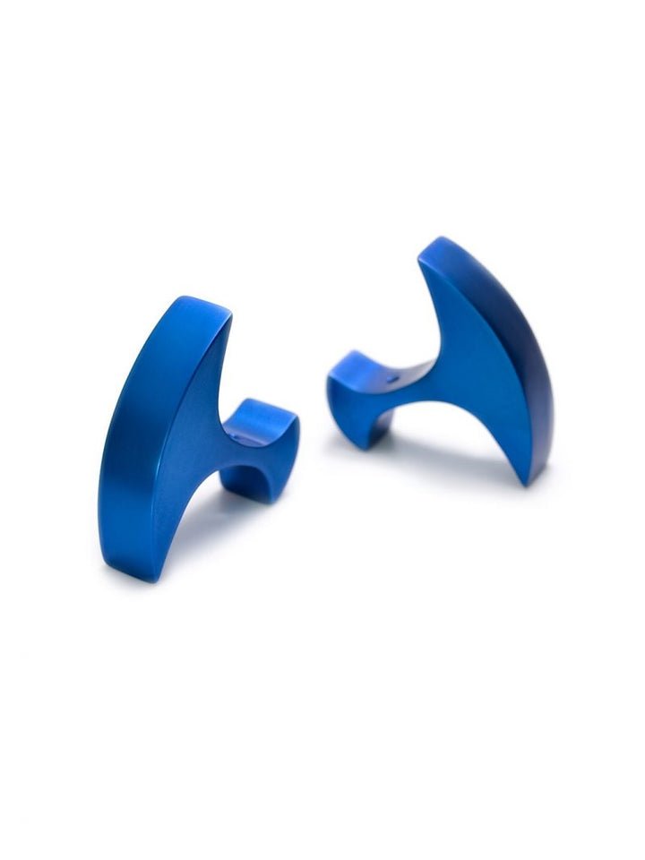 Two blue, metallic, T-shaped objects are positioned against a white background. The items have a smooth, shiny surface and a curved design, possibly indicative of modern accessories or ergonomic tools. Given their sleek appearance and anodized aluminum finish, they could be high-end cufflinks—specifically the Secant Cufflinks by Filip Vanas.