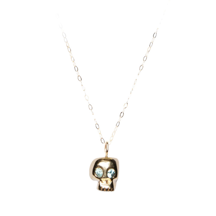 Introducing the Cosmic Boulevard 9ct Gold Memento Mori Skull Pendant, expertly crafted in our Dublin Studio. This delicate gold necklace features a chain of oval links and a pendant adorned with a small, stylized skull design. The eyes are set with blue gemstones, adding a unique touch to this exquisite piece against a plain white background.