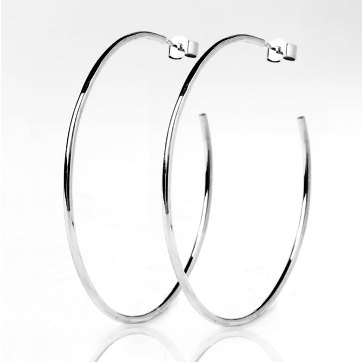 A pair of large, smooth Cosmic Thread Hoops in shiny silver metal from Cosmic Boulevard. They feature a simple and classic circular design with a small clasp at the top for fastening. The plain white background emphasizes the shiny silver hoops as the focal point of the image.