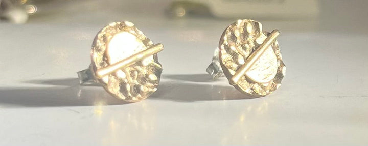 A pair of Lunar Eclipse Stud Earrings by Gallardo & Blaine Designs with circular, textured designs are displayed on a white surface. Each earring features a horizontal bar across its center, adding a unique, modern touch that echoes French elegance. The background is softly blurred.