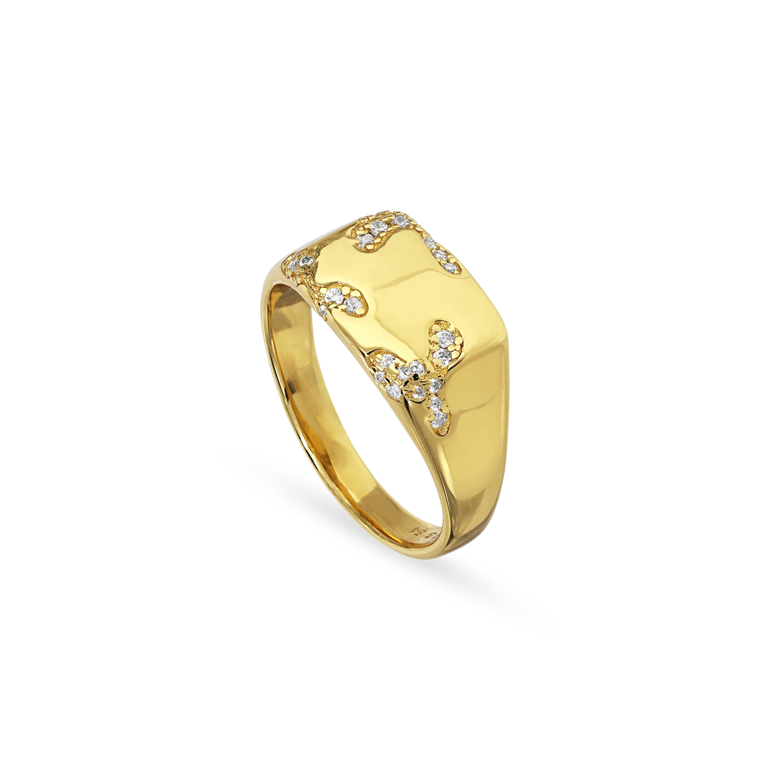The Iced Signet Ring by Jane Koenig is a gold-plated ring with a rectangular top, featuring organic branching designs and small clear gemstones—a distinctive piece of jewelry.