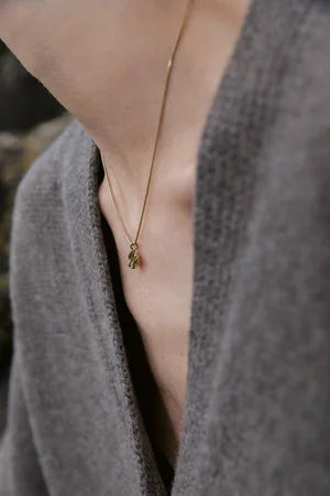 Close-up of a person wearing a soft gray sweater and the Inner Island Little Joy Necklace—a delicate gold piece with a small hand-shaped pendant—perfect for everyday wear, highlighting their neck and collarbone.