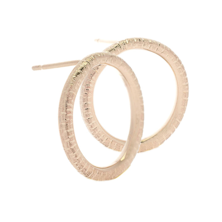 Close-up image of a pair of hand engraved gold hoop earrings with a textured surface. The Into The Light Circle Earrings 9ct Yellow Gold by Aud have a circular design and post-back closures.