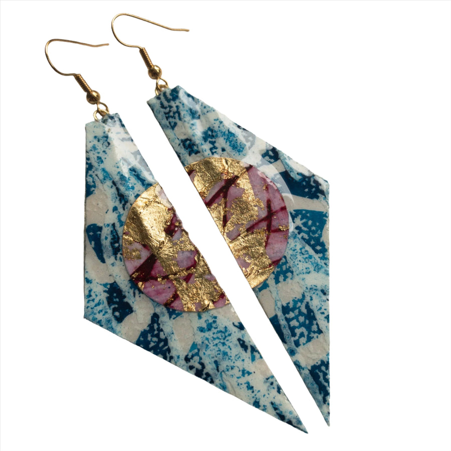 Introducing the Irma Batik Textile Earrings in Blue/Red/Gold by Rothlú. These lightweight statement earrings feature an abstract design with triangular shapes and a blue patterned background, overlaid with circular elements in vibrant red and gold hues. The textured earrings are connected to hypo-allergenic gold hooks, making them as comfortable as they are stunning.