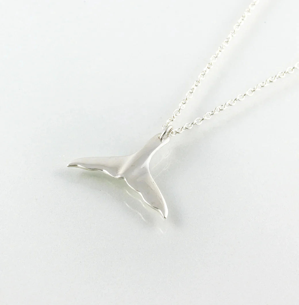 The Jennifer Kinnear Whales Tail Necklace enchants with its silver pendant reflecting light on a smooth surface, displayed on a light background. The delicate chain connects seamlessly to the whale tail fin, embodying Tarifa's breezy charm.