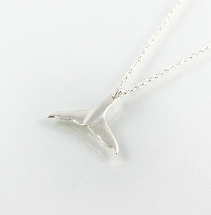 The Jennifer Kinnear Whales Tail Necklace features a striking silver pendant shaped like a whale's tail, elegantly suspended on a delicate chain, and highlighted against a plain white background to evoke Tarifa's serene beauty.