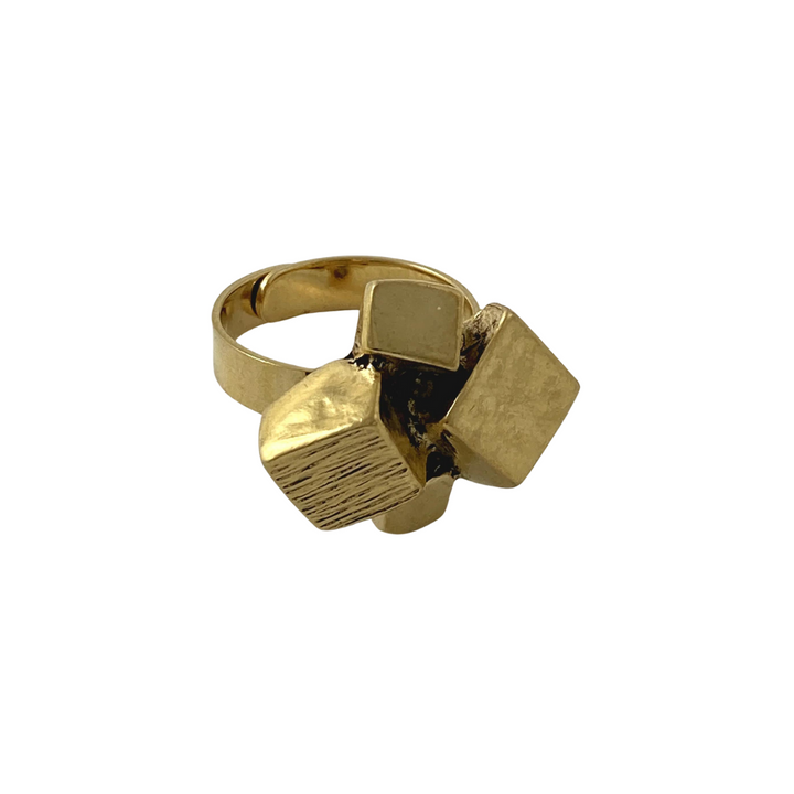 A fine Jazz Gold Plated Pewter Ring from J. Boetsch Creations featuring an abstract design with three geometric shapes: a cube, a cylindrical shape, and a rectangular prism. The shapes are arranged in a clustered formation, giving the ring a modern and artistic appearance. The smooth and polished band highlights its elegance.