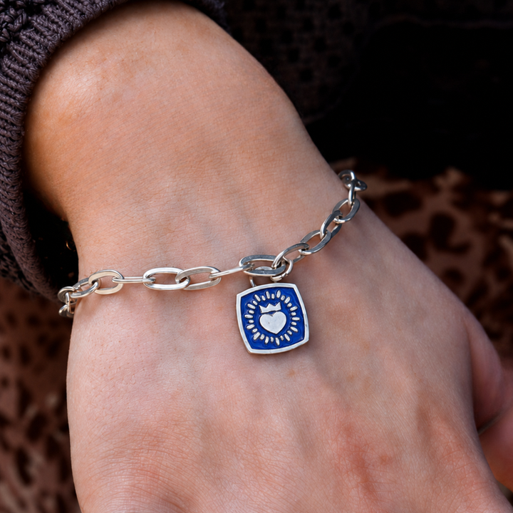 A close-up of The Collective Dublin's Double Sided Keith Haring Claddagh On Charm Bracelet on a person's wrist, paired with a brown textured sweater, highlights the timeless elegance of contemporary Irish jewelry.