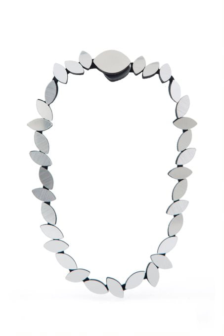 The Kate Leaves Silver Necklace by Iskin Sisters is a modern statement piece that features an arrangement of overlapping, oval-shaped silver and black mirror-like elements. These ovals vary in size and are meticulously arranged to form a symmetrical, continuous loop, creating a captivating reflective design against a white background.