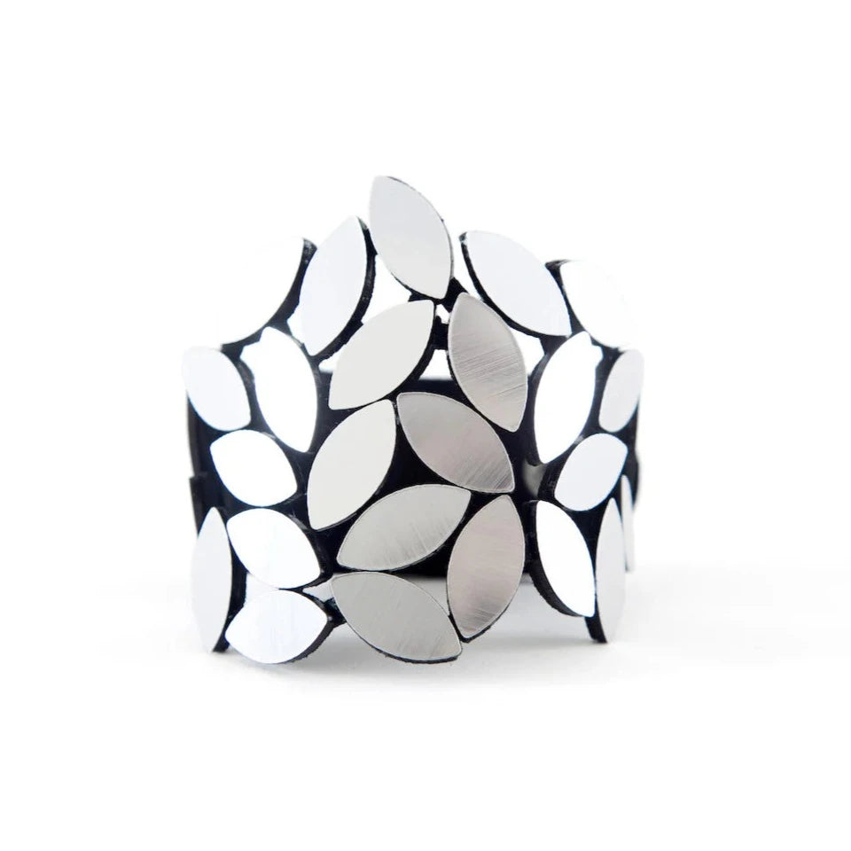 The Kate Leaves Bracelet Medium by Iskin Sisters is a striking cuff bracelet featuring an abstract design of overlapping, leaf-shaped metallic pieces. The leaves are polished and reflective, creating a modern and eye-catching accessory.