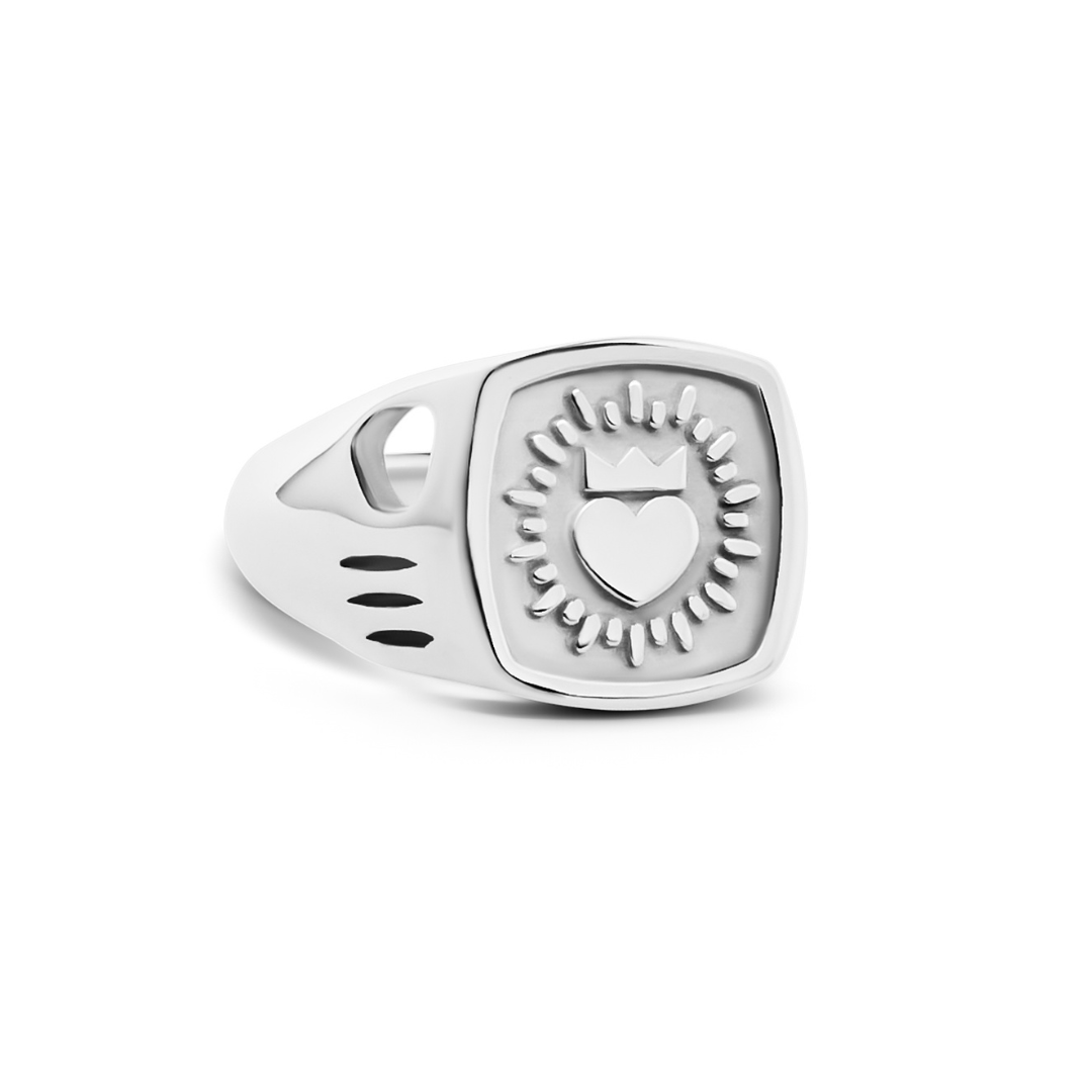 The Collective Dublin’s Keith Haring Inspired Claddagh Ring features a silver square face with an engraved heart and crown, circular accents, and cut-out band details—a modern take on Irish jewelry tradition.