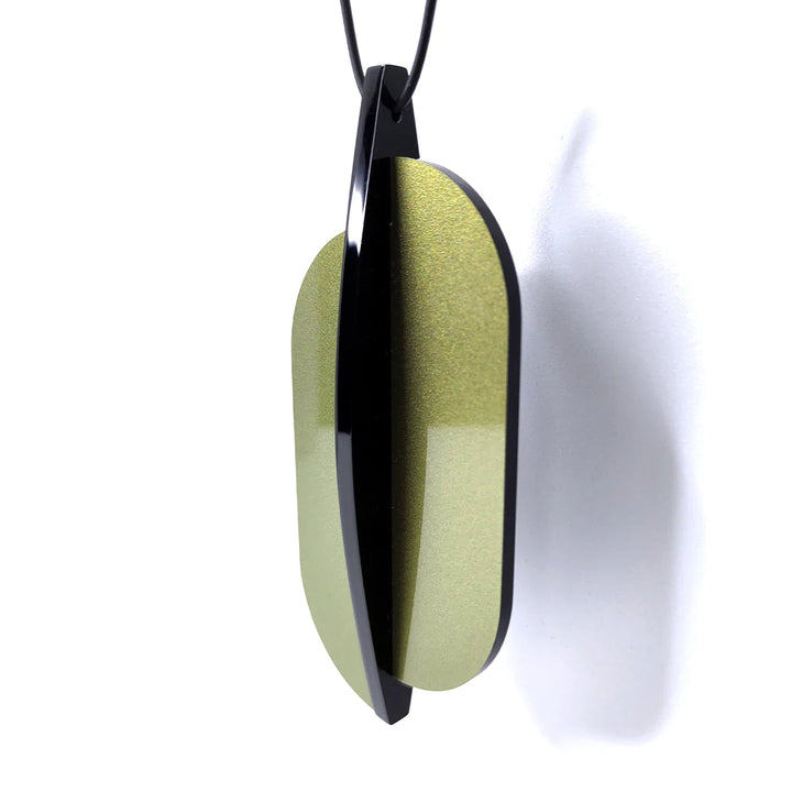 The Lars Statement Acrylic Pendant by Alex + Svet, available in a sleek modern design, hangs on a black cord. It features two overlapping elliptical pieces: one crafted from high-quality frosted acrylic with a glossy black finish and the other boasting a shimmering gold surface. This handcrafted jewelry piece casts an elegant shadow on a white background.