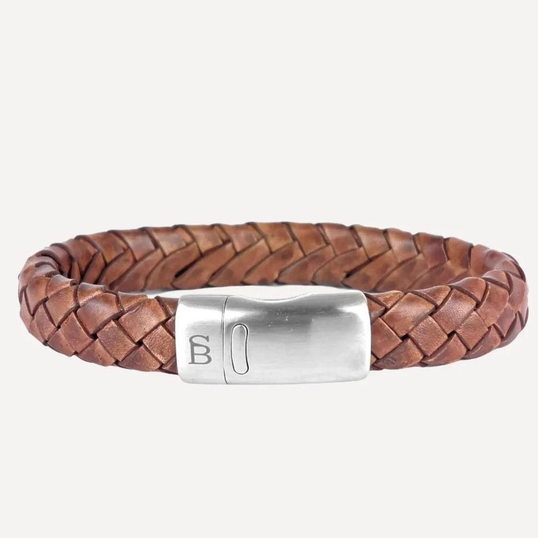 The Steel and Barnett Cornall - Caramel is a brown, genuine braided leather bracelet featuring a stainless steel clasp with an engraved design. The bracelet has a smooth and polished finish, giving it a sleek yet rustic appearance.