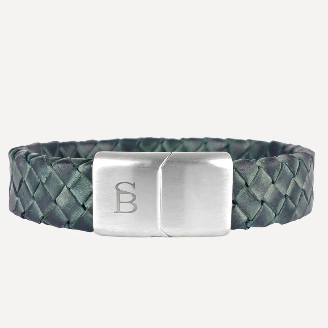 A stylish men's braided leather bracelet featuring a dark green genuine leather band with a sleek, stainless steel clasp. The clasp is engraved with a minimalist logo composed of an interlocking "B" and "D". The braided design adds texture and sophistication to the accessory. Introducing the Preston - Matte Green by Steel and Barnett.