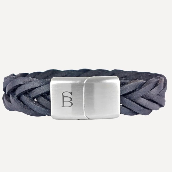 A black genuine leather bracelet with a silver clasp. The clasp features an engraved monogram with the letters "SB" on its surface. This masculine wristwear boasts a sleek and modern design, suitable for both casual and formal wear is available in the Preston - Navy style from Steel and Barnett.