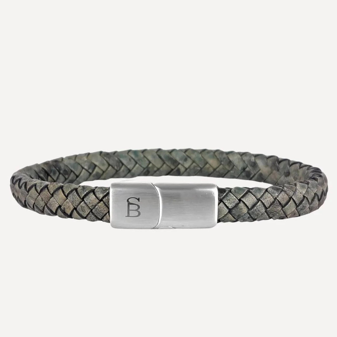 A sleek men's braided leather bracelet featuring a muted green and gray hue, complemented by a branded metal clasp and an embossed "B" logo, the Riley - Dark Green by Steel and Barnett.