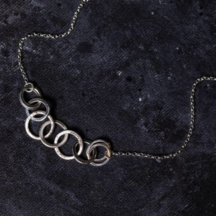 A Lynsey de Burca Carran Chain Necklace with a central design of interlocked rings displayed on a dark, textured background.