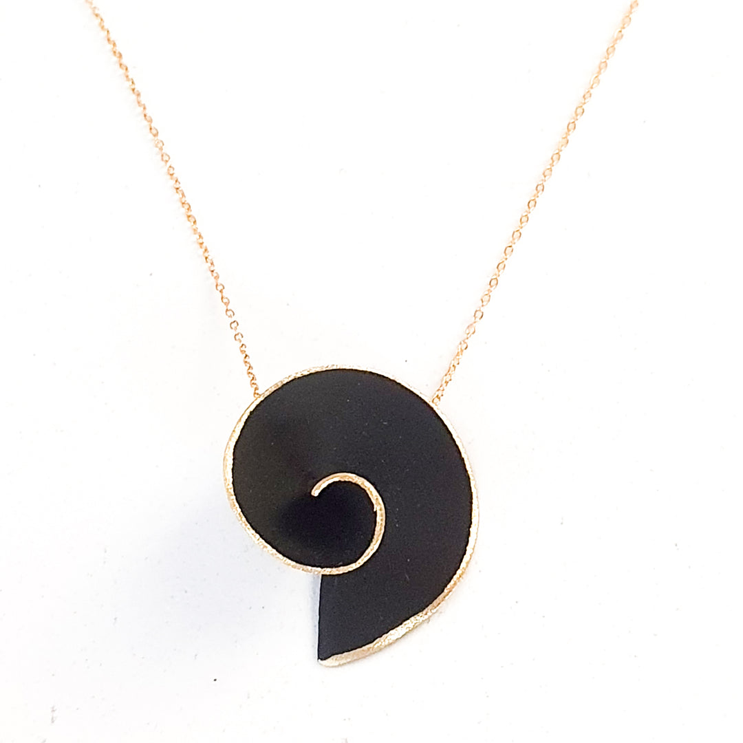 A delicate hand made necklace with a fine gold chain showcasing the Large Matt Swirl Pendant by Georgia Charal. The pendant, resembling a stylized snail shell or nautilus, features clean, smooth lines against a white background, all elegantly combined with the allure of gold plated silver.