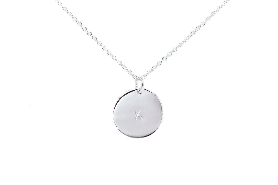 A silver necklace with a fine chain features a round, reflective pendant. The pendant has a small engraved letter "K" in the center. The minimalist design exudes elegance and simplicity, making it an ideal personalized gift. The background is white, emphasizing the Personalised Large Disc Charm in Silver by Personalised Charms.