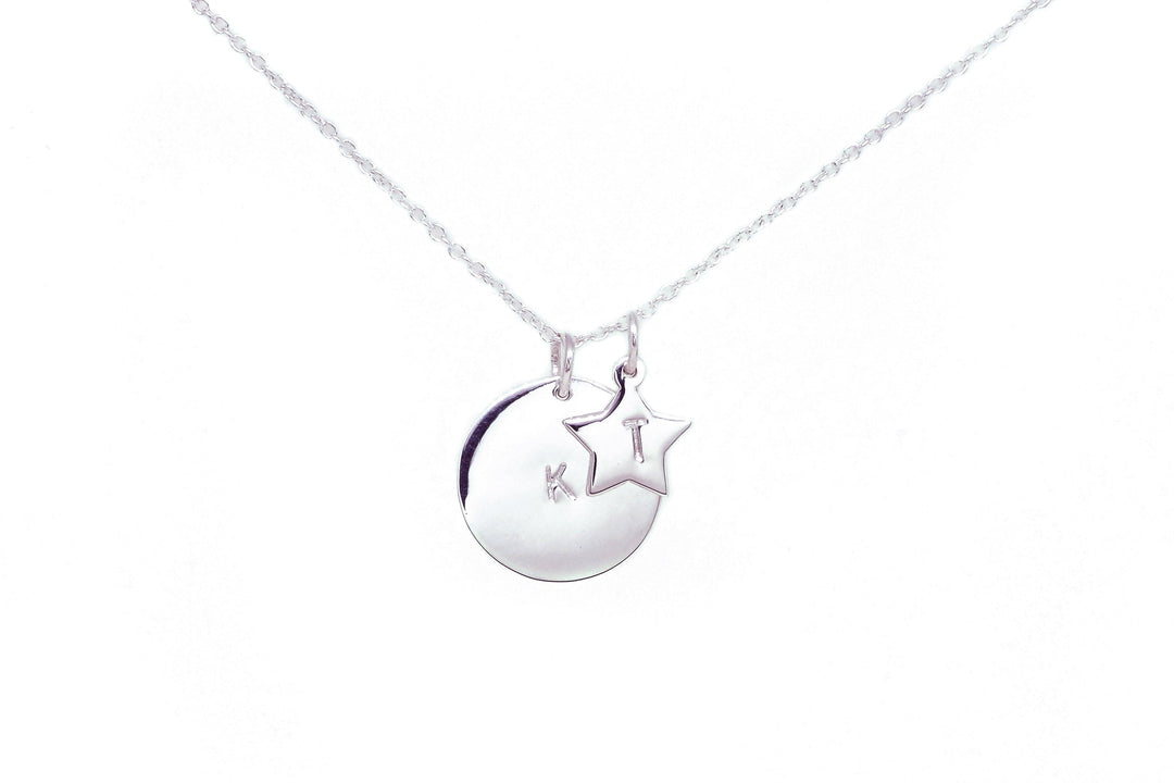 A Personalised Large Disc Charm in Silver from Personalised Charms with two sterling silver charms on a delicate chain. One pendant is a circular disc, hand-stamped with the initials "K T," and the other is a star-shaped charm. This personalized gift stands out beautifully against the plain white background.