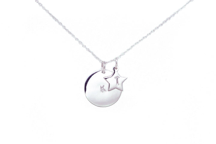 A Personalised Large Disc Charm in Silver from Personalised Charms with two sterling silver charms on a delicate chain. One pendant is a circular disc, hand-stamped with the initials "K T," and the other is a star-shaped charm. This personalized gift stands out beautifully against the plain white background.