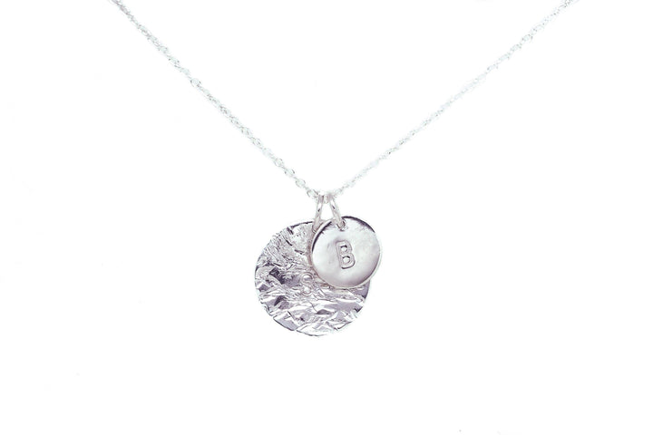 A silver necklace with a delicate chain features two round pendants. One pendant is textured with a crinkled design, and the other is smooth with the letter "B" engraved on it. The Personalised Large Disc Charm in Silver by Personalised Charms makes for a perfect personalized gift, hanging elegantly against a plain white background.