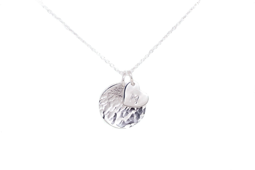 A Personalised Charms Personalised Large Disc Charm in Silver necklace with two sterling silver charms: one is a hammered circular disc, and the other is a small, smooth heart charm hand stamped with the letter "M," making it a perfect personalized gift.