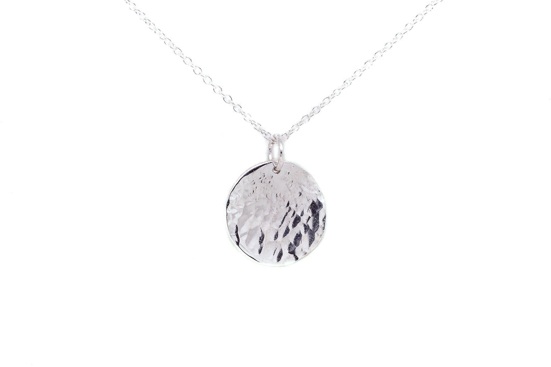 A delicate silver necklace features a textured, round pendant hanging from a fine chain. The pendant has a hammered finish and sterling silver charms, giving it a rustic and artisanal appearance. The background is plain white, highlighting the simplicity and elegance of this Personalised Large Disc Charm in Silver by Personalised Charms.