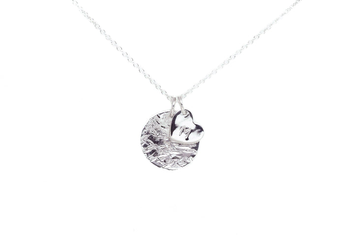 A delicate silver necklace features two pendants: a textured round disc and a polished heart charm. The chain is fine and understated, highlighting the simplicity and elegance of the sterling silver charms. Perfect as a personalized gift, the background is a clean, white backdrop. Personalised Charms presents the Personalised Large Disc Charm in Silver.
