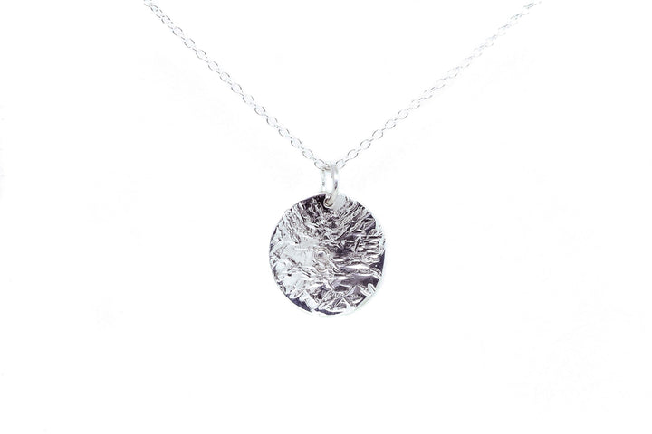 A delicate silver necklace featuring a round, hammered-texture pendant. The pendant hangs from a thin, silver chain, creating a simple yet elegant hand-stamped piece of jewelry set against a plain white background. This makes for a perfect personalized gift with timeless appeal: the Personalised Large Disc Charm in Silver by Personalised Charms.