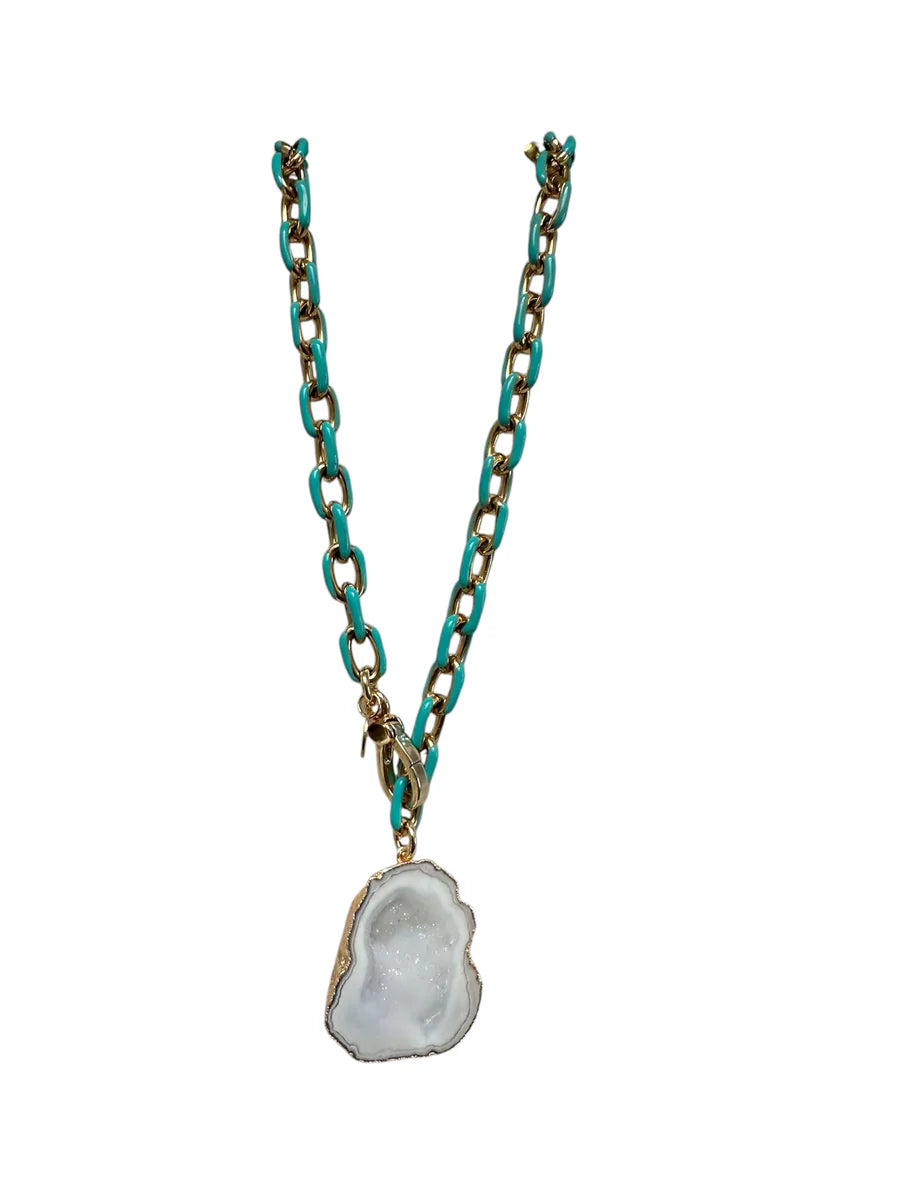 The Lazure Necklace by Aria V features a large, irregular white geode pendant edged in gold and turquoise accents, handmade in Ireland for a unique and elegant touch.