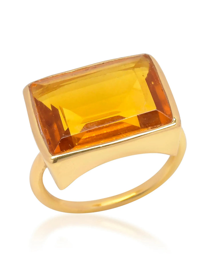 The Lenny Ring by Shyla is a 22-carat gold cocktail ring featuring a large rectangular amber-colored gemstone set in a horizontal position. The faceted gemstone sparkles brilliantly, while the simple and shiny ring band enhances its allure, making it a true statement piece.