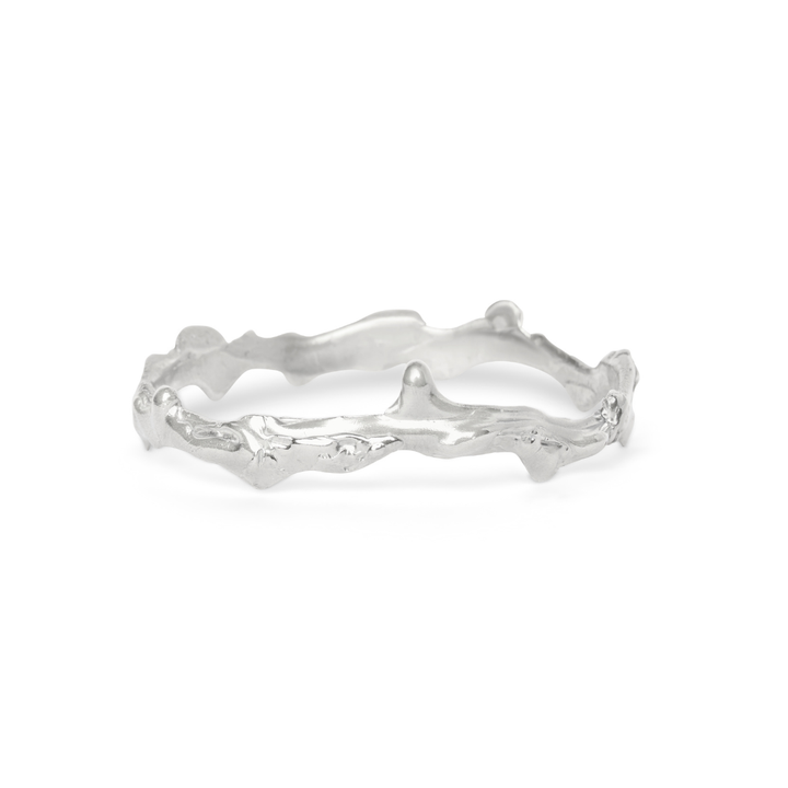The Liana Bangle by Madeleine Sculptural Jewellery features an organic, textured design inspired by intertwined branches and a natural, uneven surface. This handmade silver piece is shown on a white background.