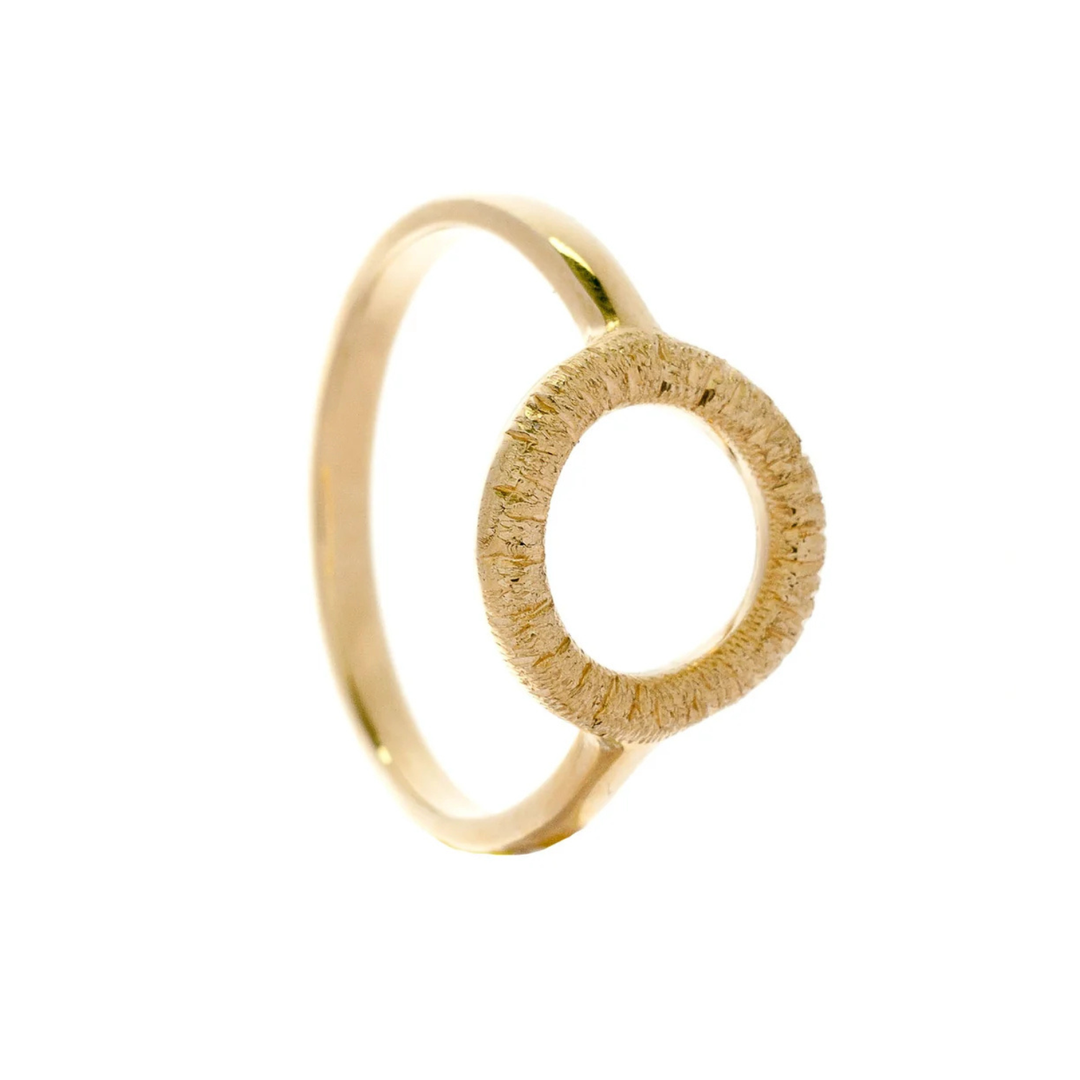 An Into The Light Mini Ring 9ct Yellow Gold with a thin, polished band and an open circle design as the centerpiece. The circle has a textured, brushed finish that contrasts with the smooth band, reflecting the coastal textures of Ireland. This piece is lovingly handmade in Audrey’s home workshop and is part of her Aud ring collection.