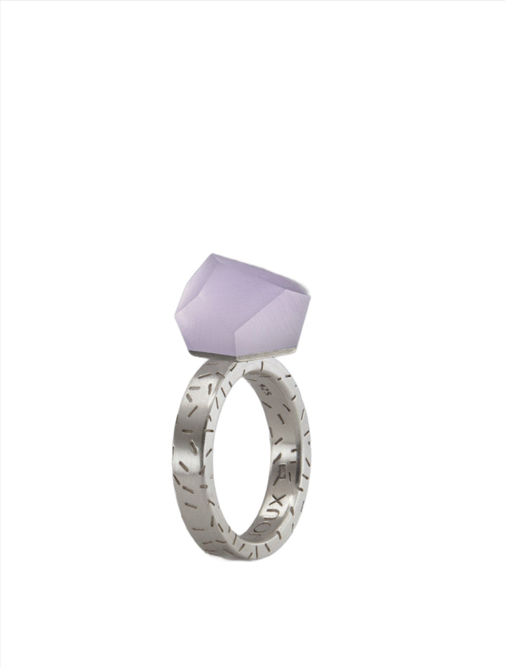 A Fruit Bijoux Fruit Bijoux Ring Top VU Crystals Lilac Purple featuring a geometric design on the band and a large, lavender gemstone mounted on top. The gemstone is faceted, adding a modern and elegant touch to the jewelry piece. The background is white.