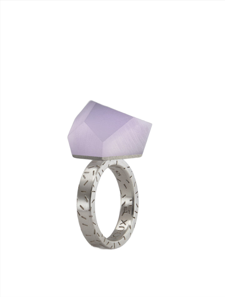 A Fruit Bijoux Fruit Bijoux Ring Top VU Crystals Lilac Purple with a wide band featuring intricate, engraved patterns. Atop the band sits a large, faceted, light-purple gemstone with an angular, geometric shape. The ring top is set against a plain white background.