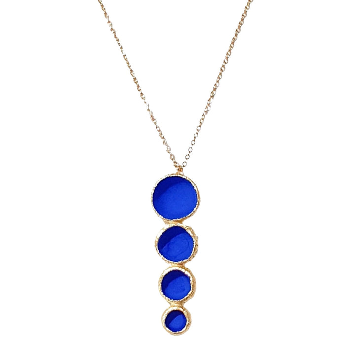 The Long Matt Pendant by Georgia Charal is a handmade necklace with a gold-plated chain, featuring four vertically arranged cobalt blue stones that decrease in size from top to bottom, each elegantly outlined in gold.