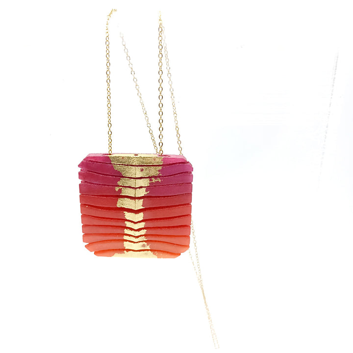 A Tochu-De Long Square Wave Necklace in Fuchsia & Orange hangs from a delicate gold chain. The 3D-printed nylon pendant features a textured, ribbed design and a gradient color pattern, transitioning from dark pink at the top to bright red at the bottom.