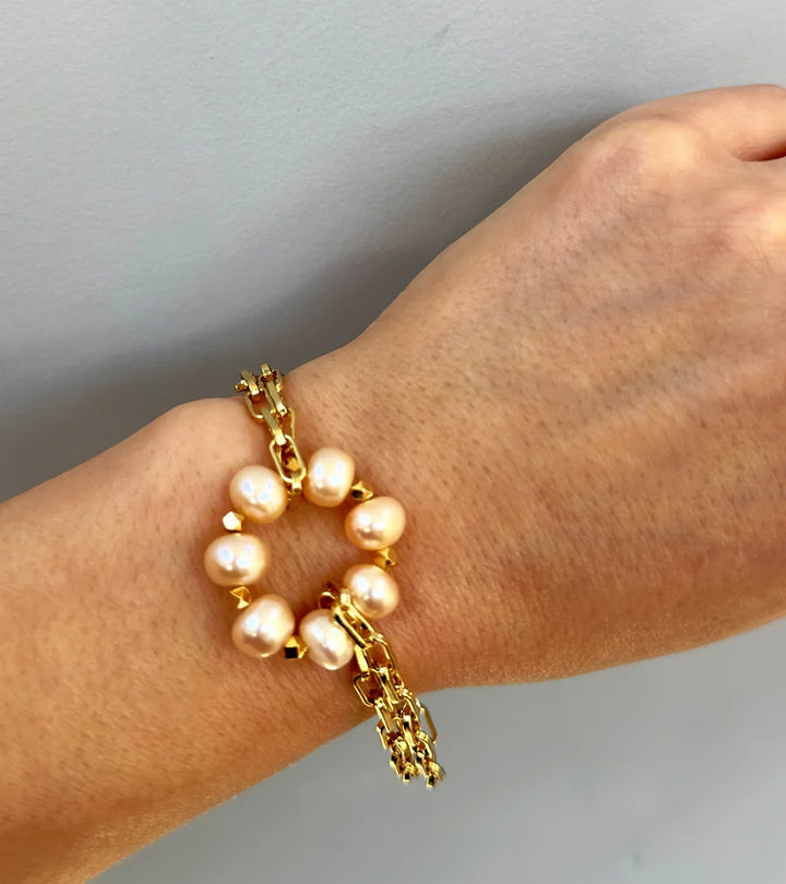 The Lunaire Pearl Bracelet by Aria V, featuring a circular arrangement of white pearls and handmade in Ireland, is showcased on a wrist against a light grey background.