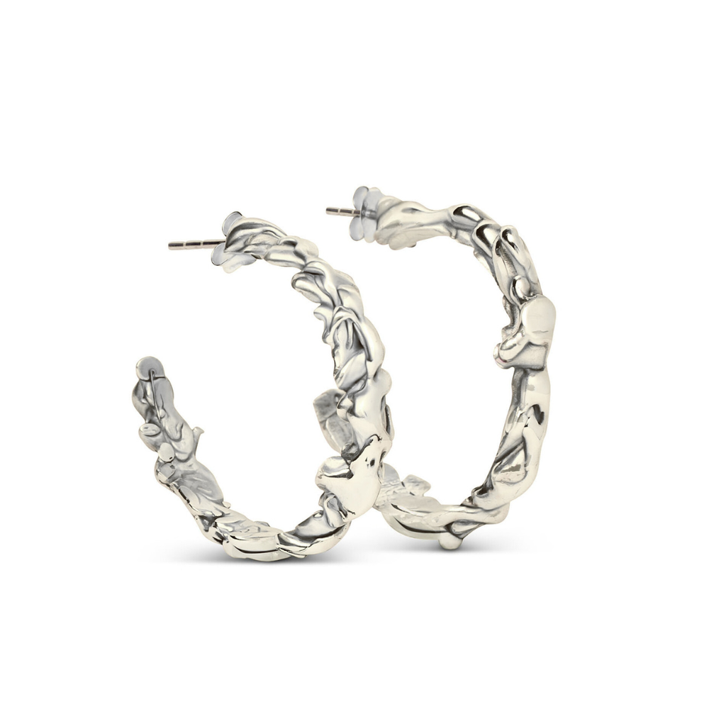 The Molten Hoops Large by Madeleine Sculptural Jewellery are silver hoop earrings with a textured, wavy design, reminiscent of hand-carved pieces, displayed upright against a white background.